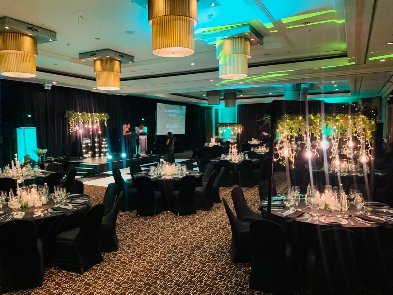 Wide view of a corporate awards banquet with greenery centerpieces and candle-lit tables