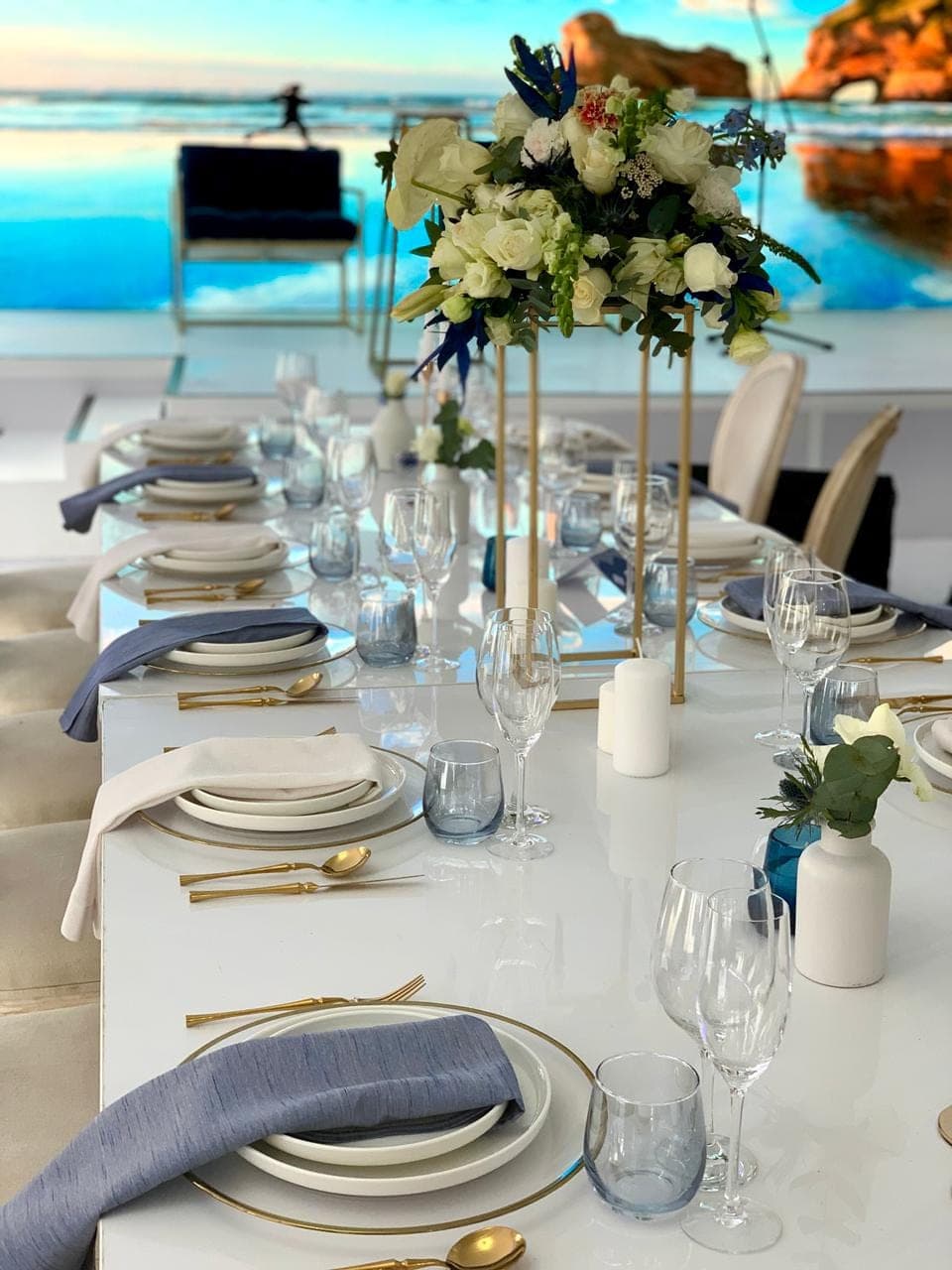Beach mural intimate dinner tablescape with tall white florals and gold accents