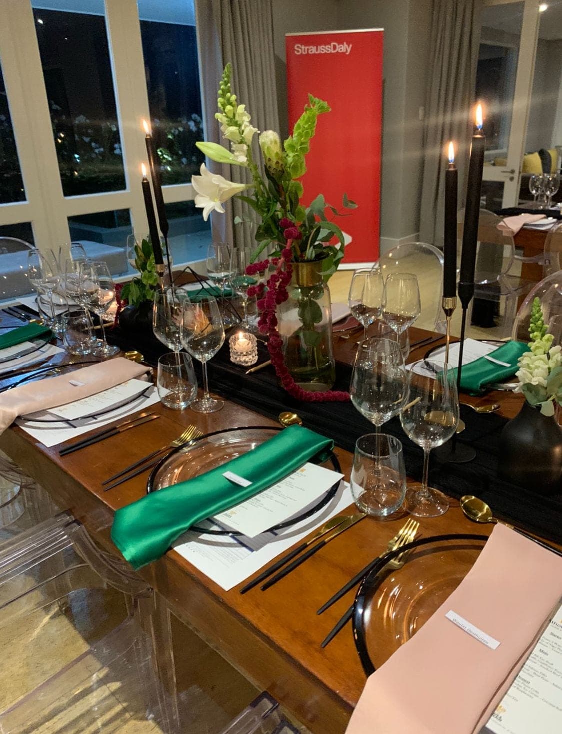 Candle-lit corporate dinner with rich greens, pinks, and branded backdrop