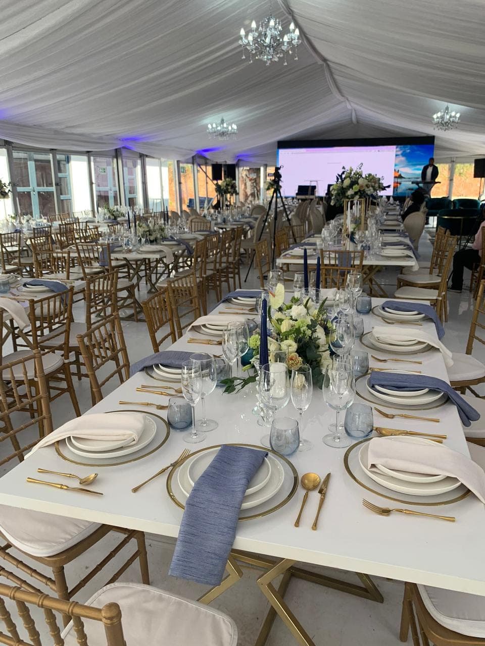 Marquee tent event setup with gold chiavari chairs and long elegant tablescapes