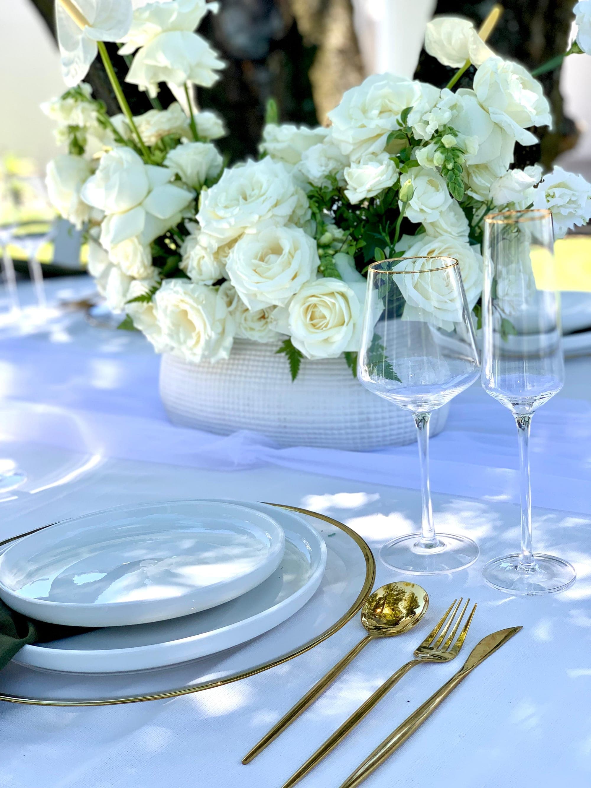 Close-up of a white rose centerpiece with gold flatware on a celebration table