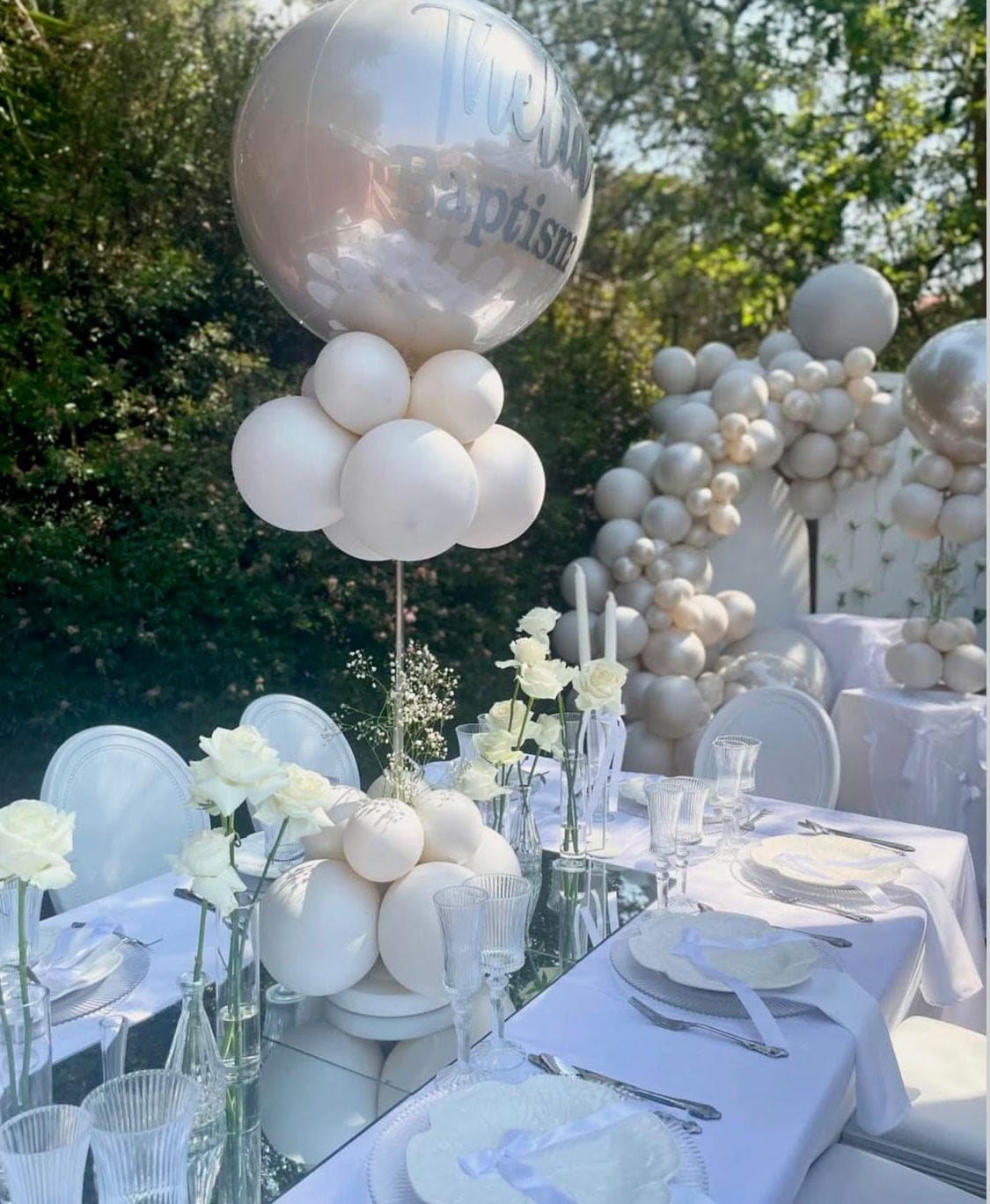 All-white outdoor baptism tablescape with a clear personalised balloon and white balloon arch