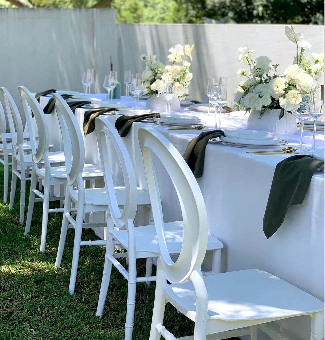 Outdoor white tablescape with white oval-back chairs, black napkins, and white rose centerpieces