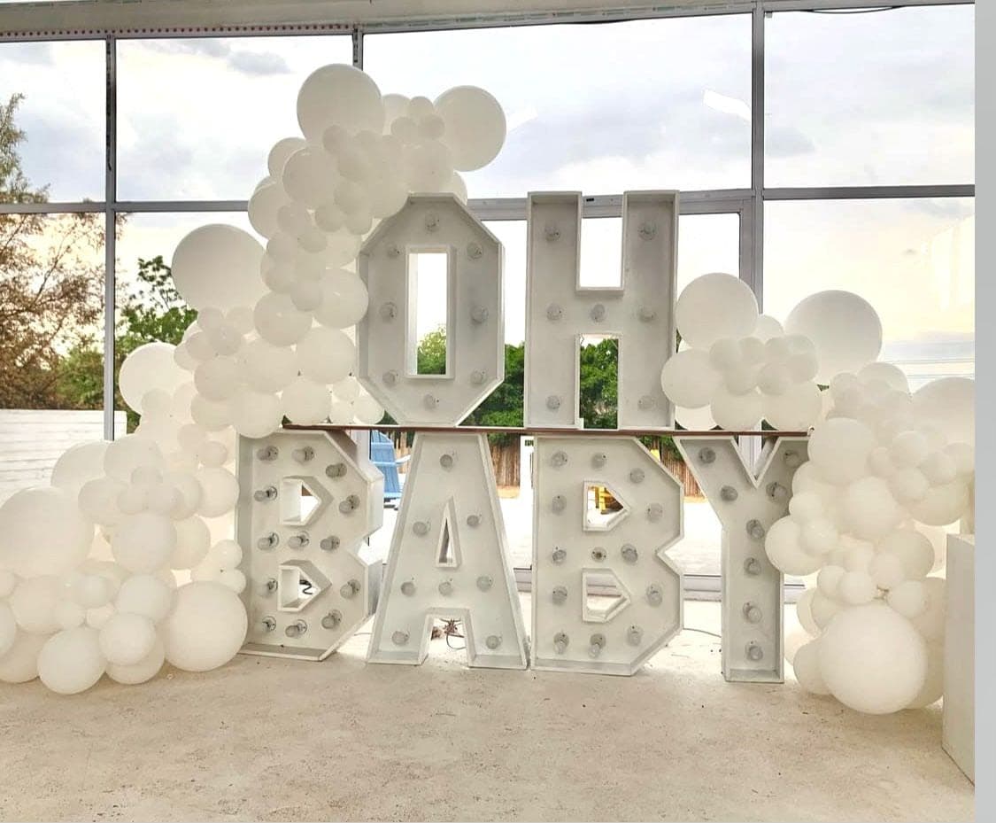Oversized illuminated 'OH BABY' marquee letters with a white balloon arch for a baby shower