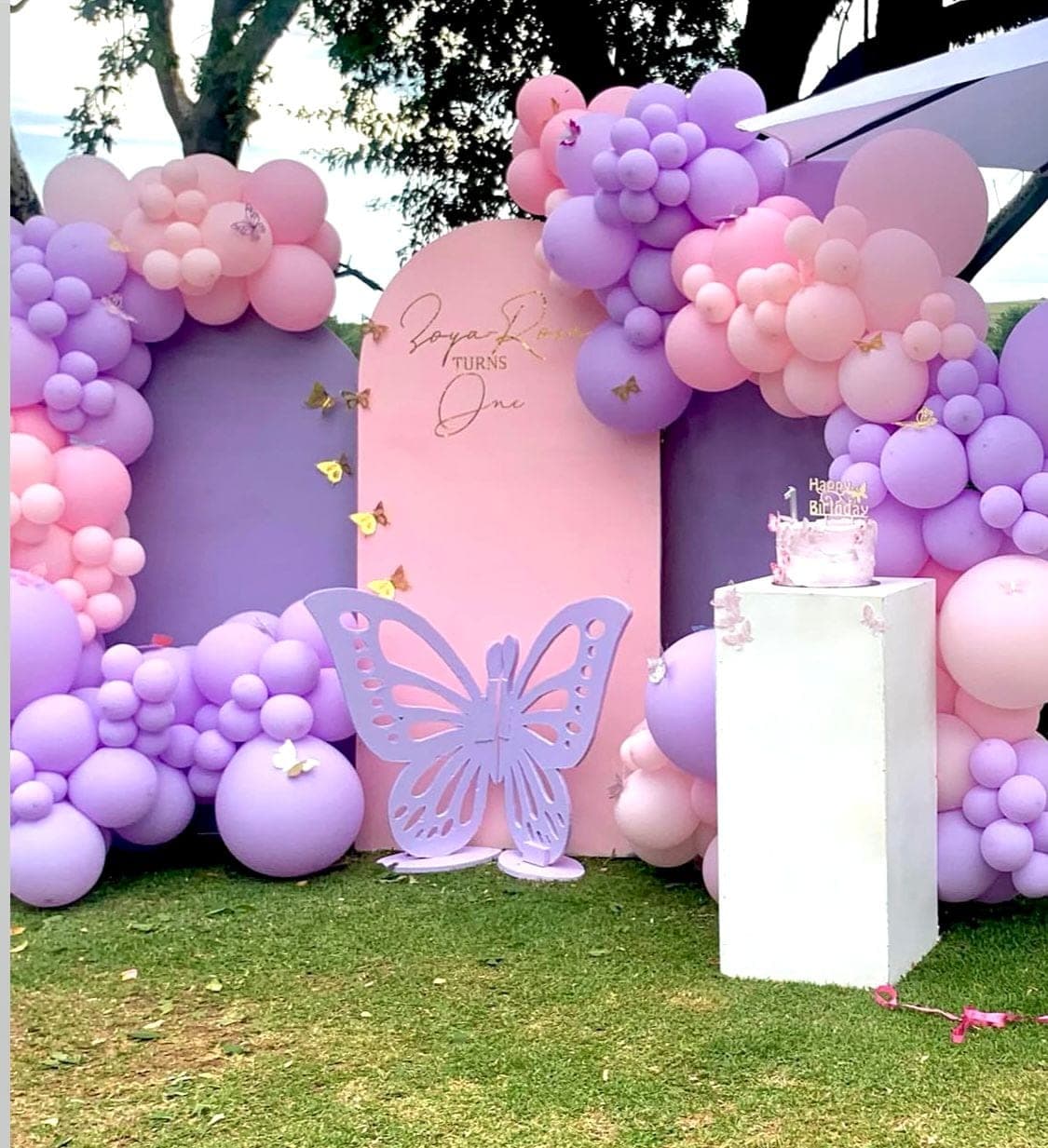 Pink and purple butterfly-themed first birthday backdrop with pastel balloon arch and butterfly cutout